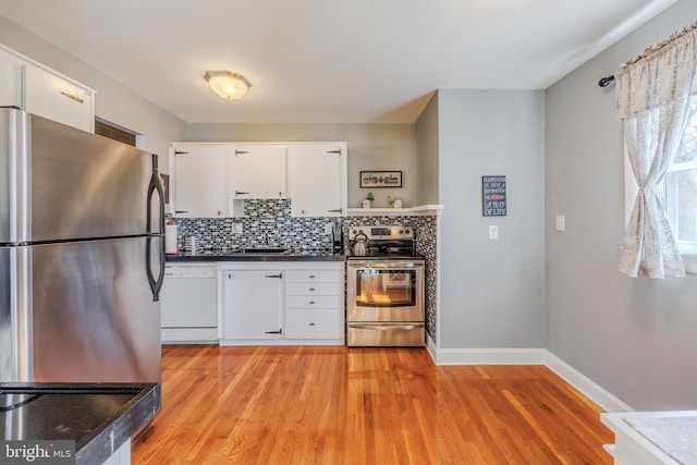 kitchen featuring stainless steel appliances, dark countertops, decorative backsplash, light wood-style floors, and white cabinetry