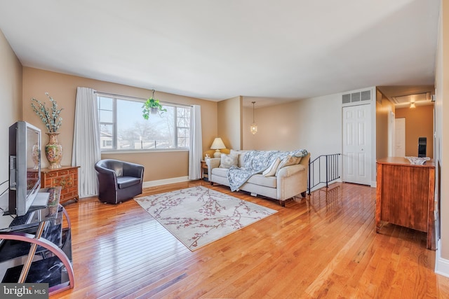 living area with light wood-type flooring, attic access, visible vents, and baseboards