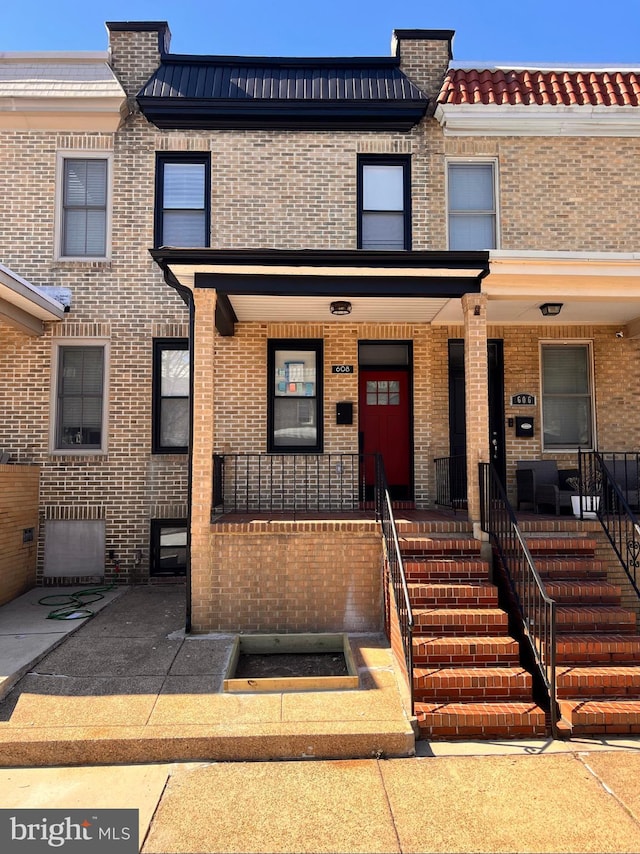 multi unit property featuring covered porch, a tiled roof, and brick siding