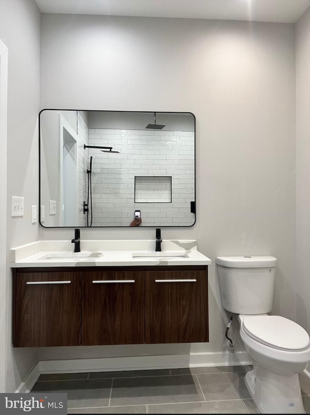 bathroom featuring toilet, double vanity, a sink, and tiled shower