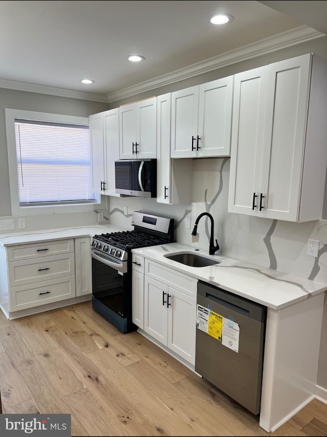 kitchen with light wood-style flooring, ornamental molding, stainless steel appliances, and a sink