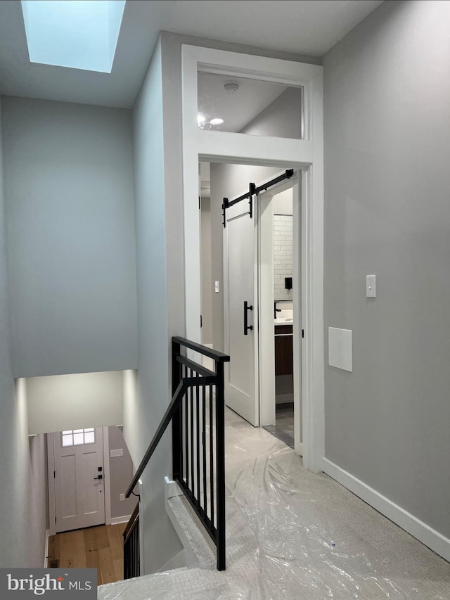 hall with a skylight, a barn door, baseboards, wood finished floors, and an upstairs landing