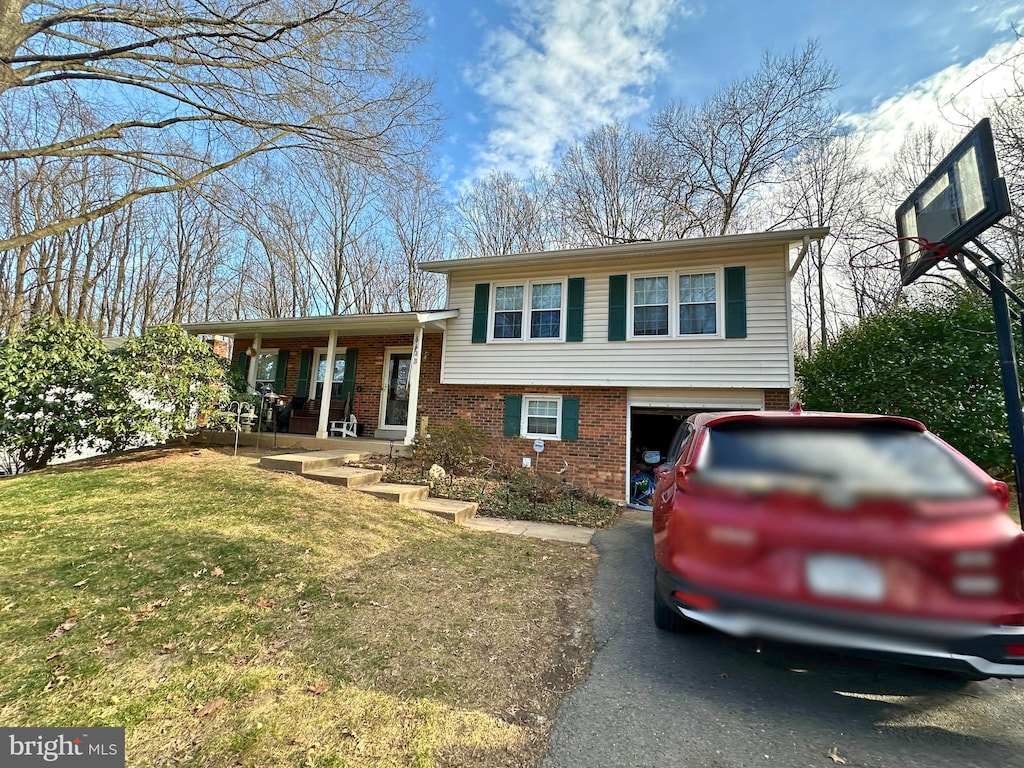 tri-level home with driveway, a garage, a front lawn, a porch, and brick siding