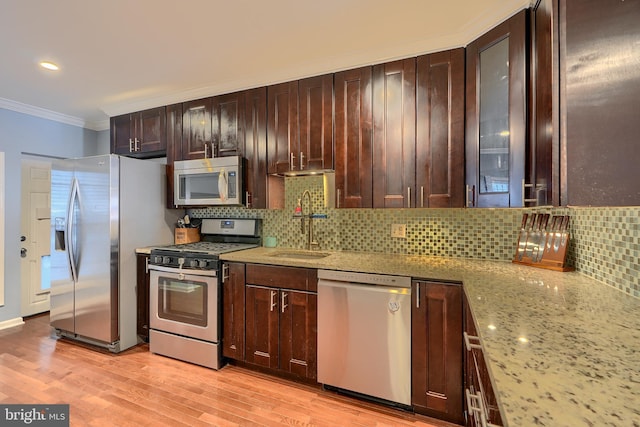 kitchen featuring light wood finished floors, appliances with stainless steel finishes, crown molding, and a sink