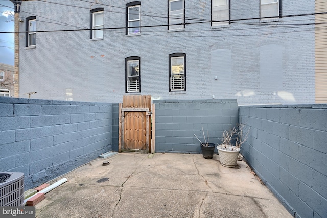 view of property exterior featuring a patio, brick siding, a fenced backyard, and a gate