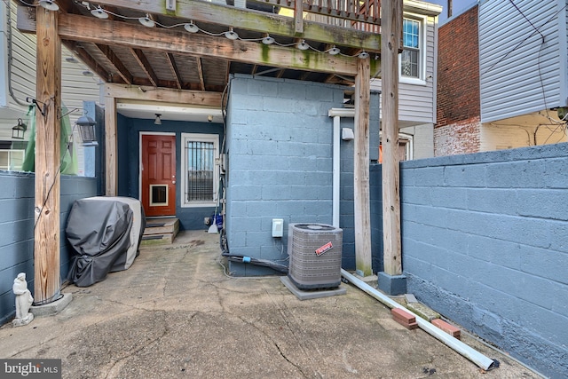 property entrance with central air condition unit, a patio, concrete block siding, and fence