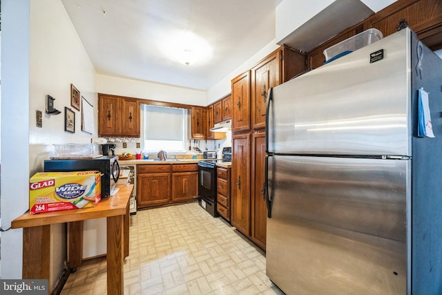 kitchen with electric range, under cabinet range hood, freestanding refrigerator, brown cabinetry, and light countertops