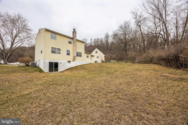 back of property with central air condition unit, a lawn, a chimney, and fence