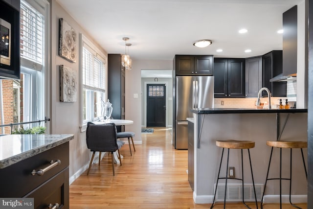 kitchen featuring light stone countertops, a breakfast bar, light wood-style flooring, freestanding refrigerator, and tasteful backsplash