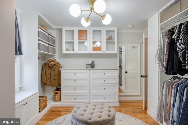 spacious closet featuring light wood-type flooring and an inviting chandelier