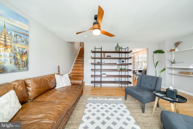 living area with a ceiling fan, stairway, wood finished floors, and baseboards