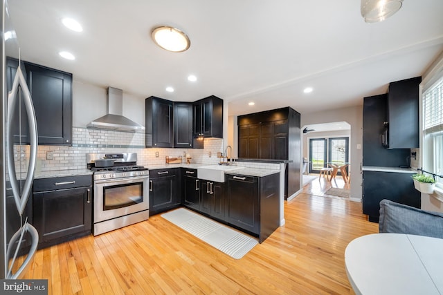 kitchen with a sink, stainless steel appliances, backsplash, and wall chimney range hood