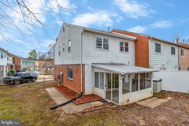 back of property with a sunroom, brick siding, fence, and a gate