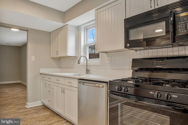 kitchen featuring light wood finished floors, light countertops, decorative backsplash, black appliances, and baseboards