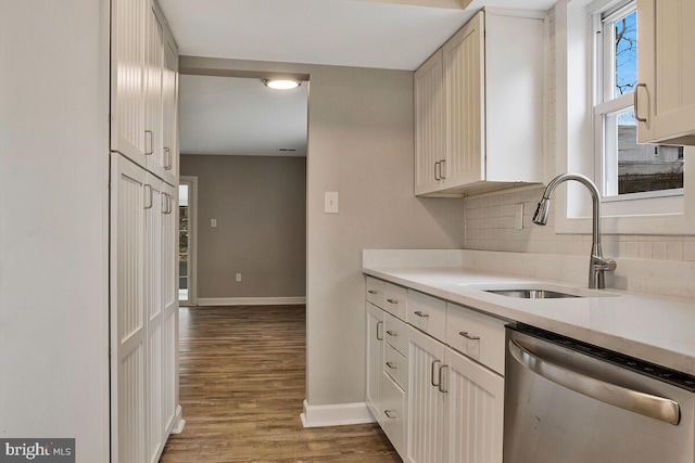 kitchen featuring light countertops, decorative backsplash, stainless steel dishwasher, a sink, and wood finished floors