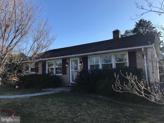 ranch-style home featuring brick siding, a chimney, and a front lawn