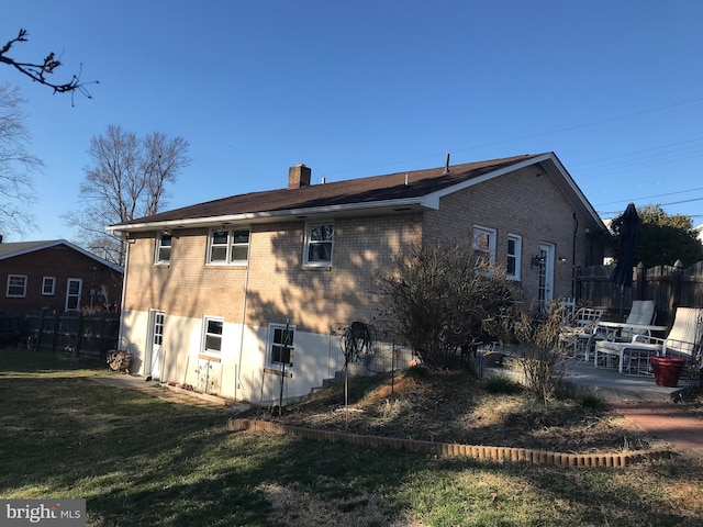 rear view of house featuring brick siding, a chimney, a lawn, and fence