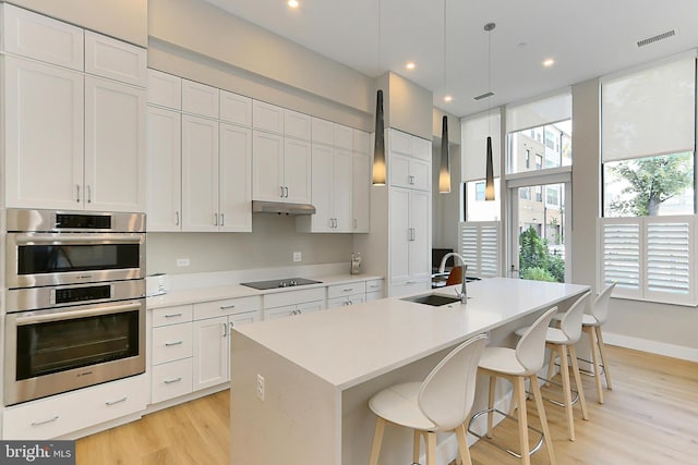 kitchen featuring double oven, black electric cooktop, under cabinet range hood, a sink, and light wood-type flooring