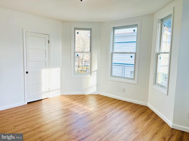 unfurnished room with light wood-style floors, a wealth of natural light, and baseboards