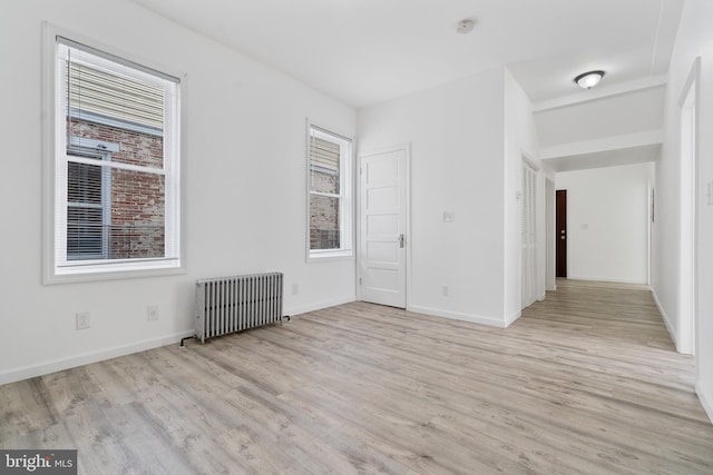 unfurnished bedroom featuring baseboards, multiple windows, radiator heating unit, and light wood-style floors