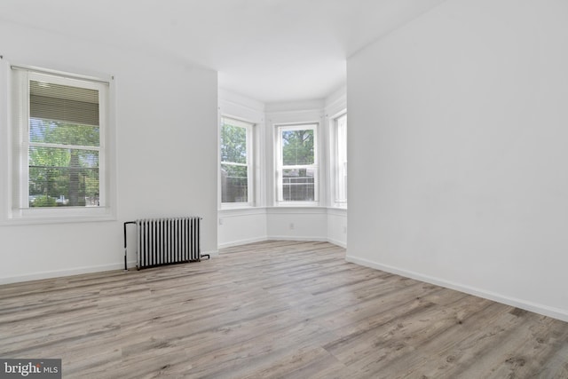 unfurnished room with radiator, a healthy amount of sunlight, baseboards, and wood finished floors