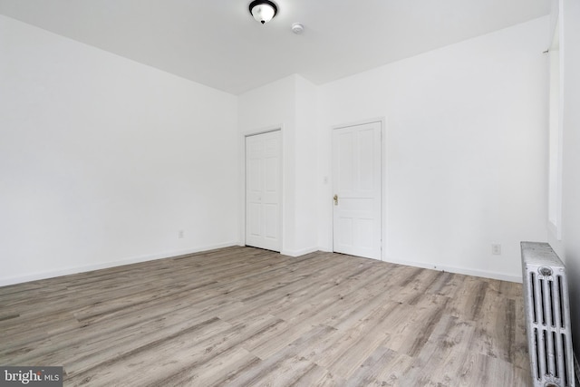 unfurnished bedroom with baseboards, wood finished floors, and radiator