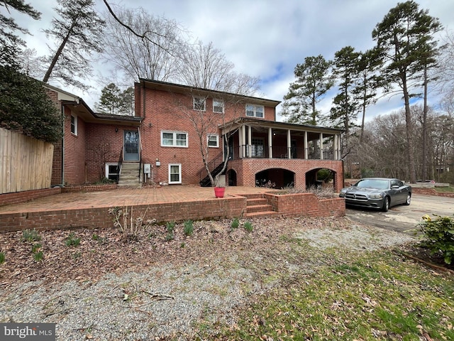 rear view of property featuring a patio area, a sunroom, brick siding, and stairway