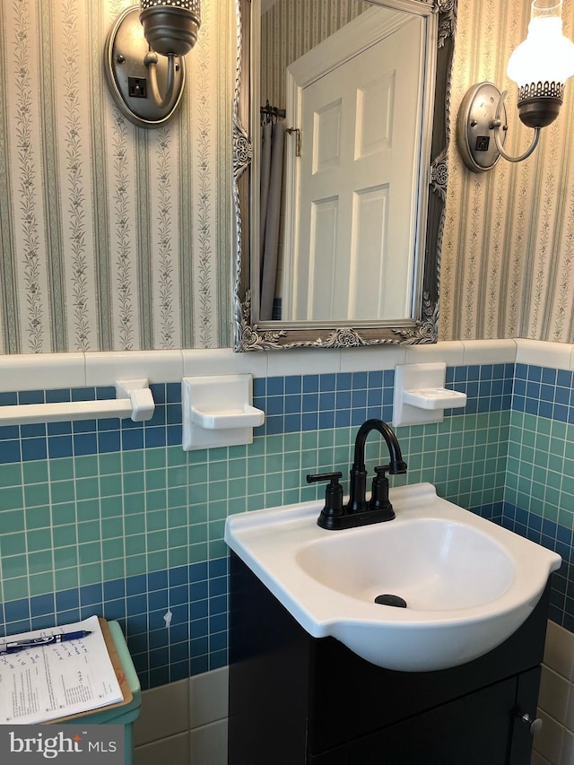 bathroom featuring wainscoting, vanity, tile walls, and wallpapered walls