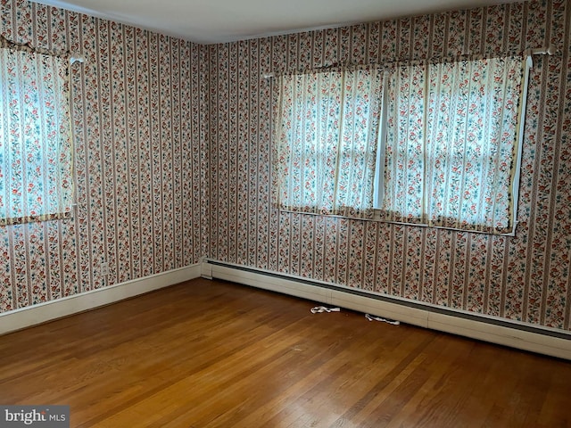 empty room featuring baseboards, wallpapered walls, baseboard heating, and wood finished floors