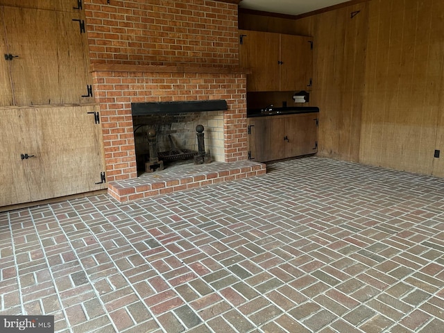 unfurnished living room with brick floor, a fireplace, a sink, and wooden walls