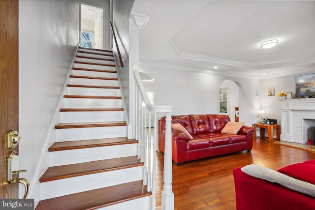 staircase with a fireplace, wood finished floors, arched walkways, and ornamental molding