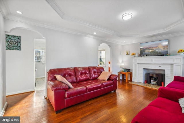 living area featuring arched walkways, ornamental molding, a tray ceiling, and wood-type flooring