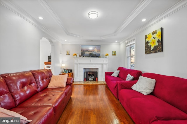 living room with ornamental molding, a tray ceiling, wood finished floors, arched walkways, and a brick fireplace