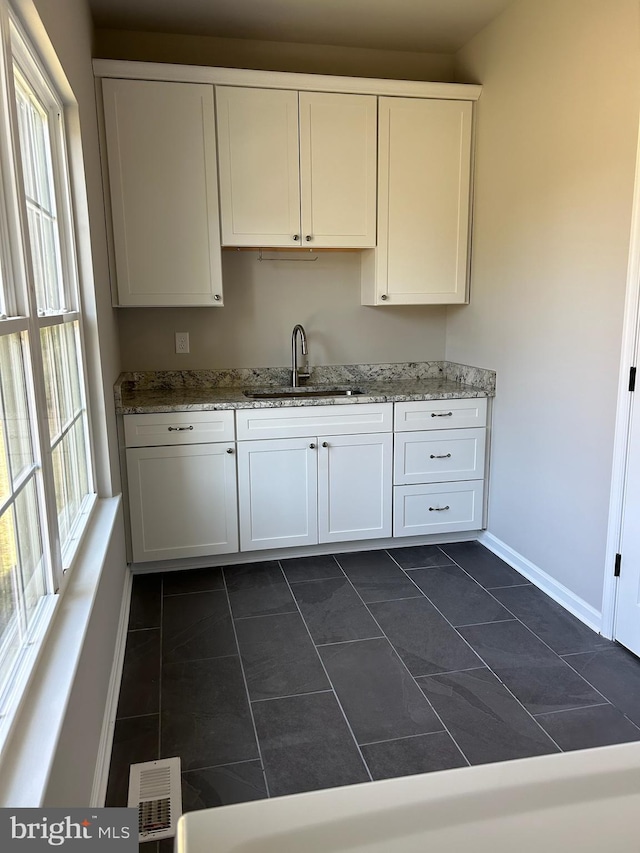 kitchen featuring a sink, visible vents, baseboards, white cabinets, and light stone countertops