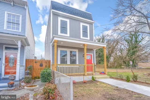 view of front of home with mansard roof, fence, board and batten siding, covered porch, and roof with shingles