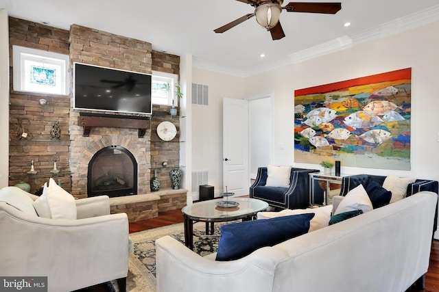 living area with visible vents, crown molding, a stone fireplace, and wood finished floors