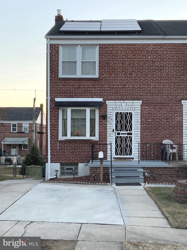 view of front of house with a chimney, fence, solar panels, and brick siding