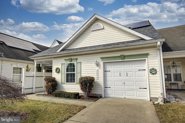 view of front of home with a garage, driveway, roof mounted solar panels, and a shingled roof