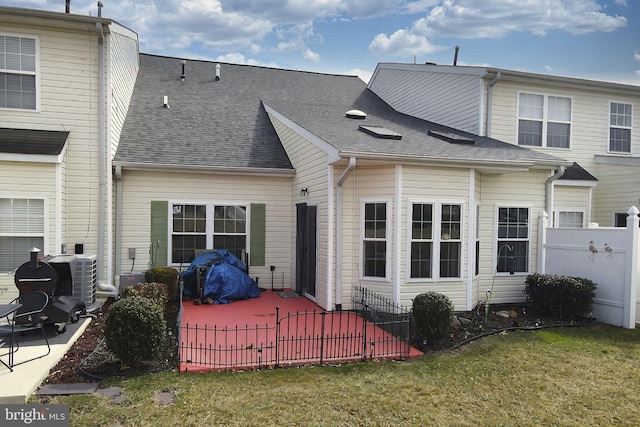 rear view of house with roof with shingles, fence, a lawn, and a patio