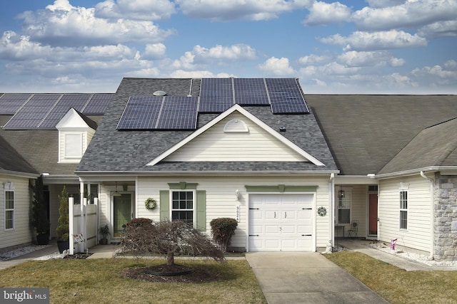 view of property featuring a garage, driveway, roof mounted solar panels, and roof with shingles