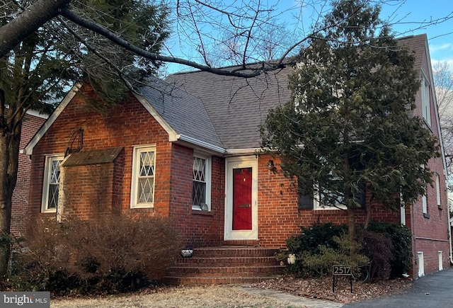 view of front facade with brick siding, entry steps, and a shingled roof