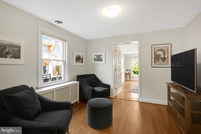 living area with visible vents, baseboards, radiator heating unit, and hardwood / wood-style flooring