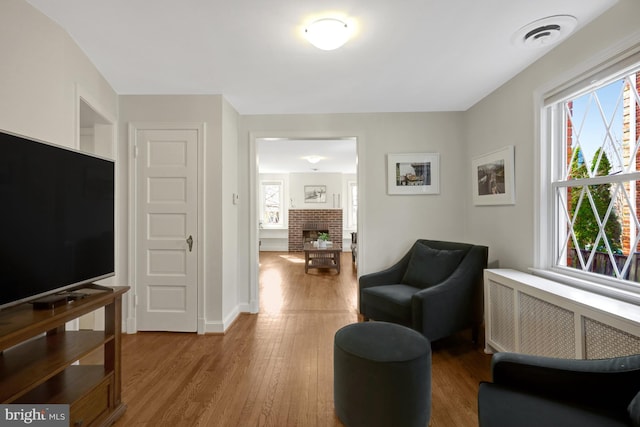 living area featuring radiator, wood finished floors, visible vents, baseboards, and a fireplace