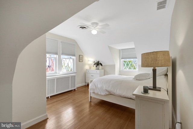 bedroom with radiator, wood finished floors, visible vents, baseboards, and vaulted ceiling