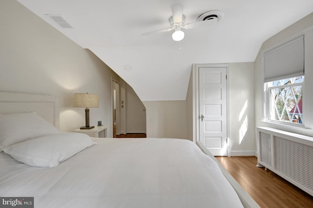 bedroom featuring vaulted ceiling, radiator heating unit, wood finished floors, and visible vents