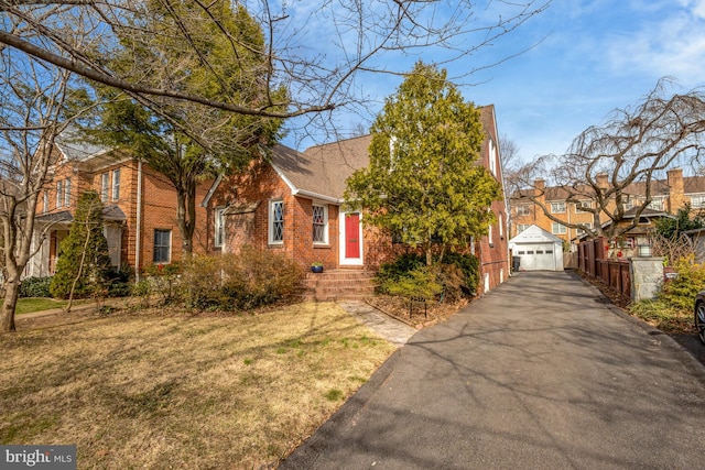 view of front facade with brick siding, aphalt driveway, a front yard, a garage, and an outdoor structure