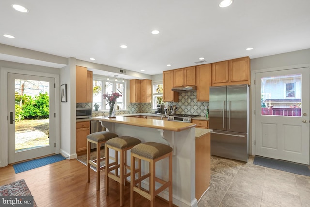 kitchen with backsplash, a kitchen island, under cabinet range hood, light countertops, and stainless steel appliances