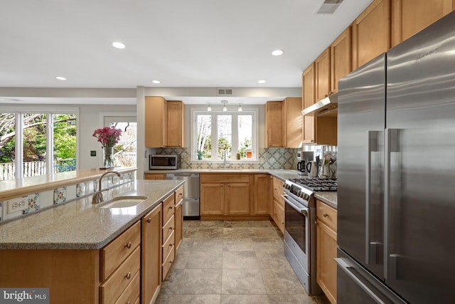 kitchen featuring tasteful backsplash, visible vents, light stone counters, stainless steel appliances, and a sink