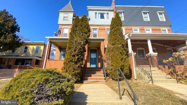 view of front of property with a porch, a high end roof, brick siding, and mansard roof