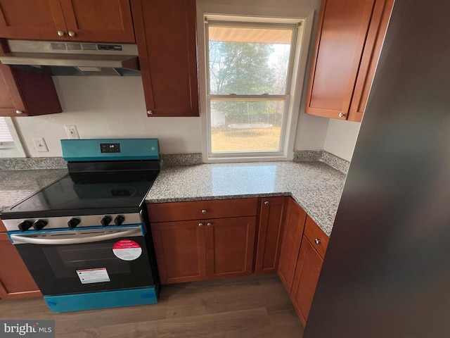 kitchen featuring light wood-type flooring, under cabinet range hood, electric range, and brown cabinetry